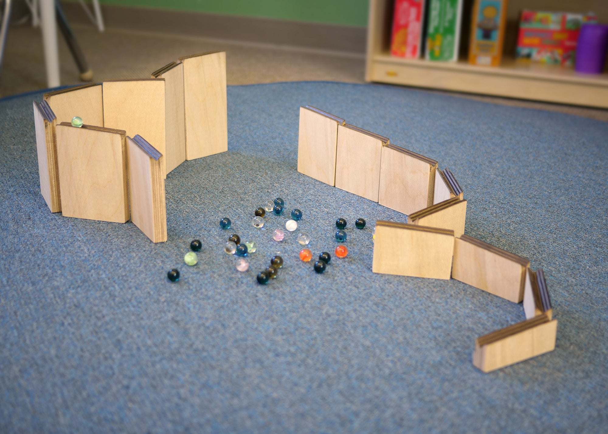 Customizable wooden marble maze ramps arranged on a blue carpet with a collection of colorful glass marbles.