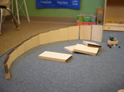 Curved wooden marble maze ramps arranged on a blue carpet with loose marbles nearby.