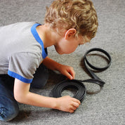 Child building a track with a flexible black rubber marble ramp on a gray carpet.