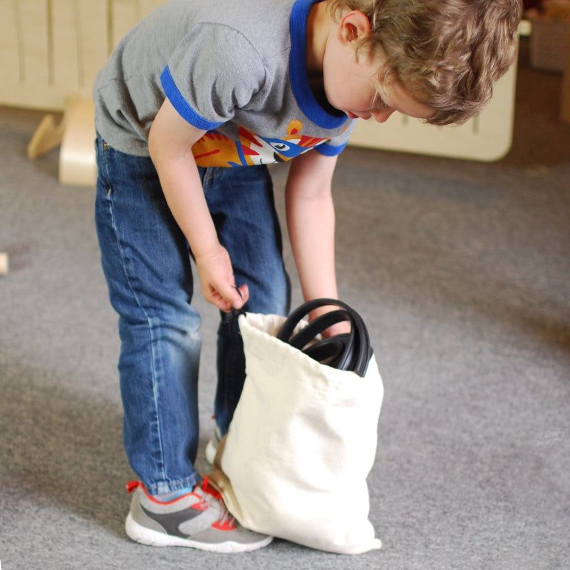 Child packing flexible black rubber marble tracks into a white canvas drawstring storage bag.