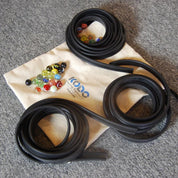 Flexible black rubber marble tracks coiled on a canvas storage bag with a collection of colorful glass marbles.