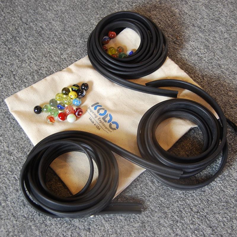 Flexible black rubber marble tracks coiled on a canvas storage bag with a collection of colorful glass marbles.