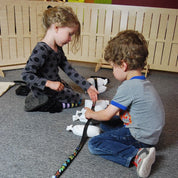 Two children building a marble track with a flexible black rubber ramp and small white weighted bags on a grey carpet.
