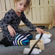A child building a marble track using a flexible black rubber ramp supported by wooden blocks and white sandbags.