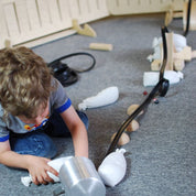 Child building a black rubber marble ramp track supported by wooden blocks and white fabric weights on a carpeted floor.