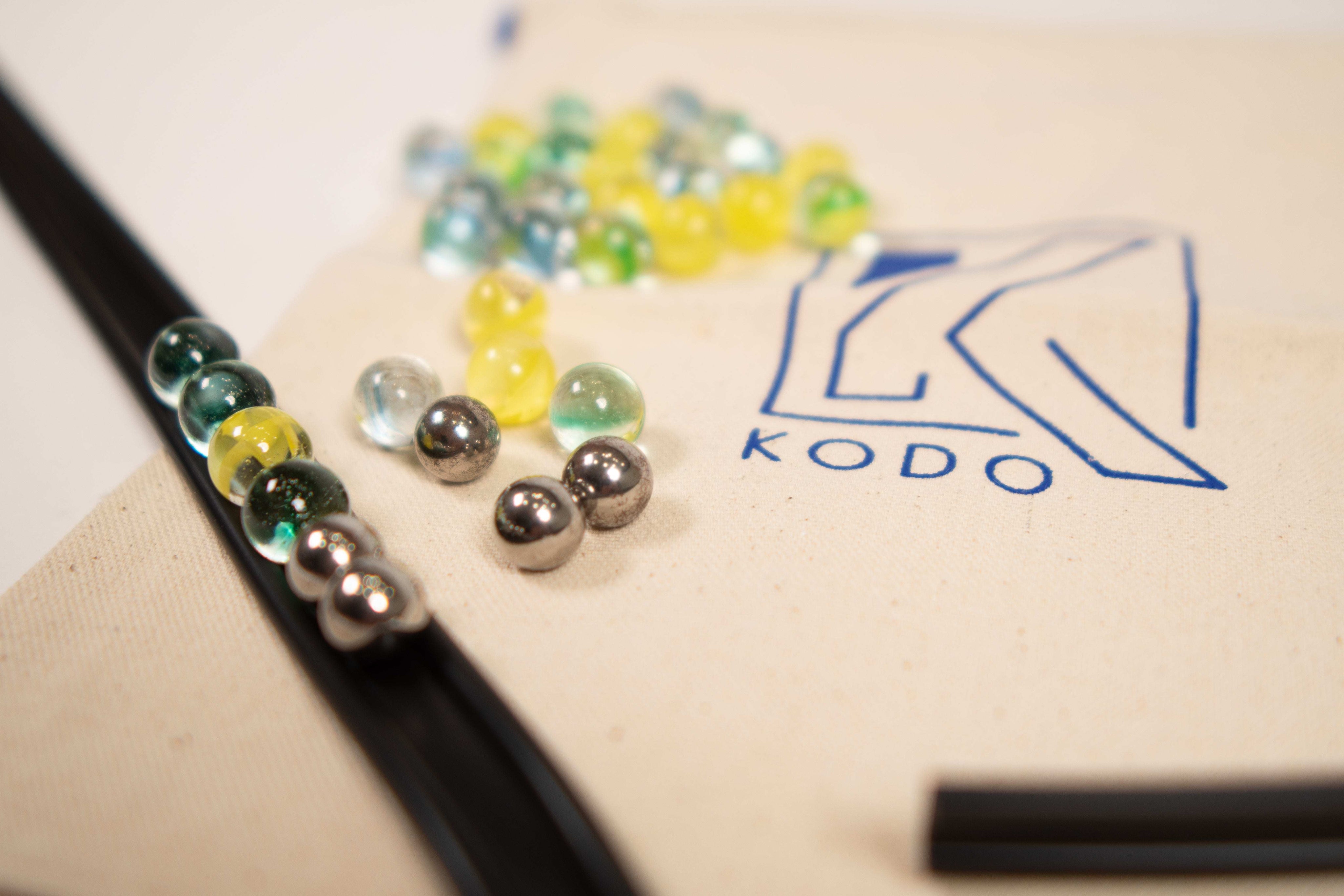 Black rubber marble ramp track with assorted glass and metal marbles on a Kodo branded canvas storage bag.