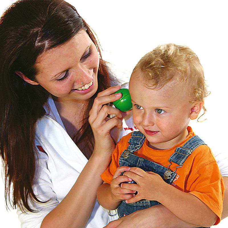 Woman holding a green Melody Ball to a toddler's ear to demonstrate the auditory STEM learning toy.