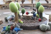 Clear round Messy Material Tray filled with wood chips, felt trees, and small animal figures for sensory play.