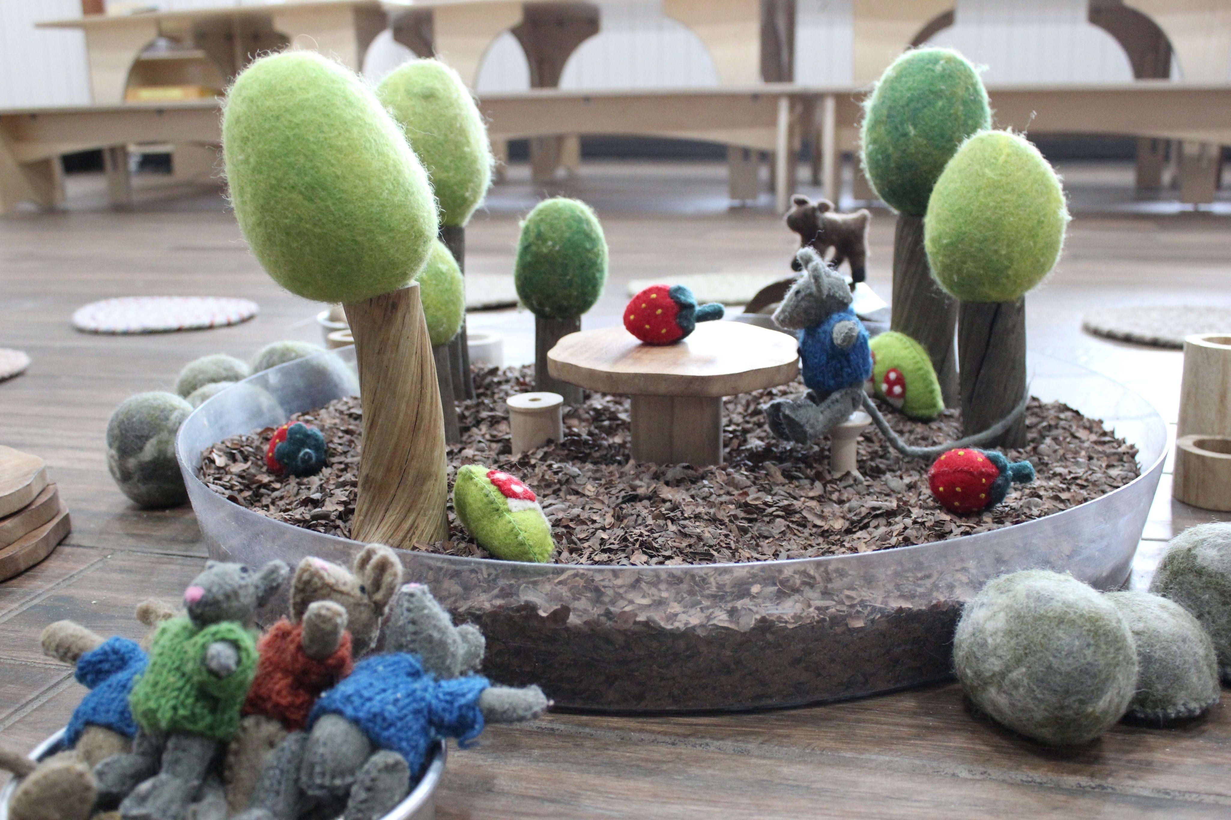 Clear round Messy Material Tray filled with wood chips, felt trees, and small animal figures for sensory play.