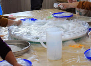 Clear, circular Messy Material Tray filled with soapy water and foam for sensory play on a classroom table.