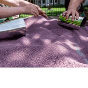 Two shiny stainless steel cups being used as molds in a pile of purple kinetic sand by children's hands.