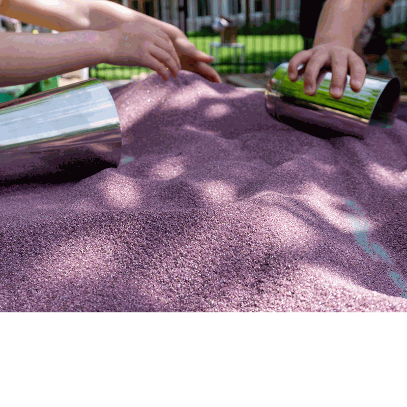 Two shiny stainless steel cups being used as molds in a pile of purple kinetic sand by children's hands.