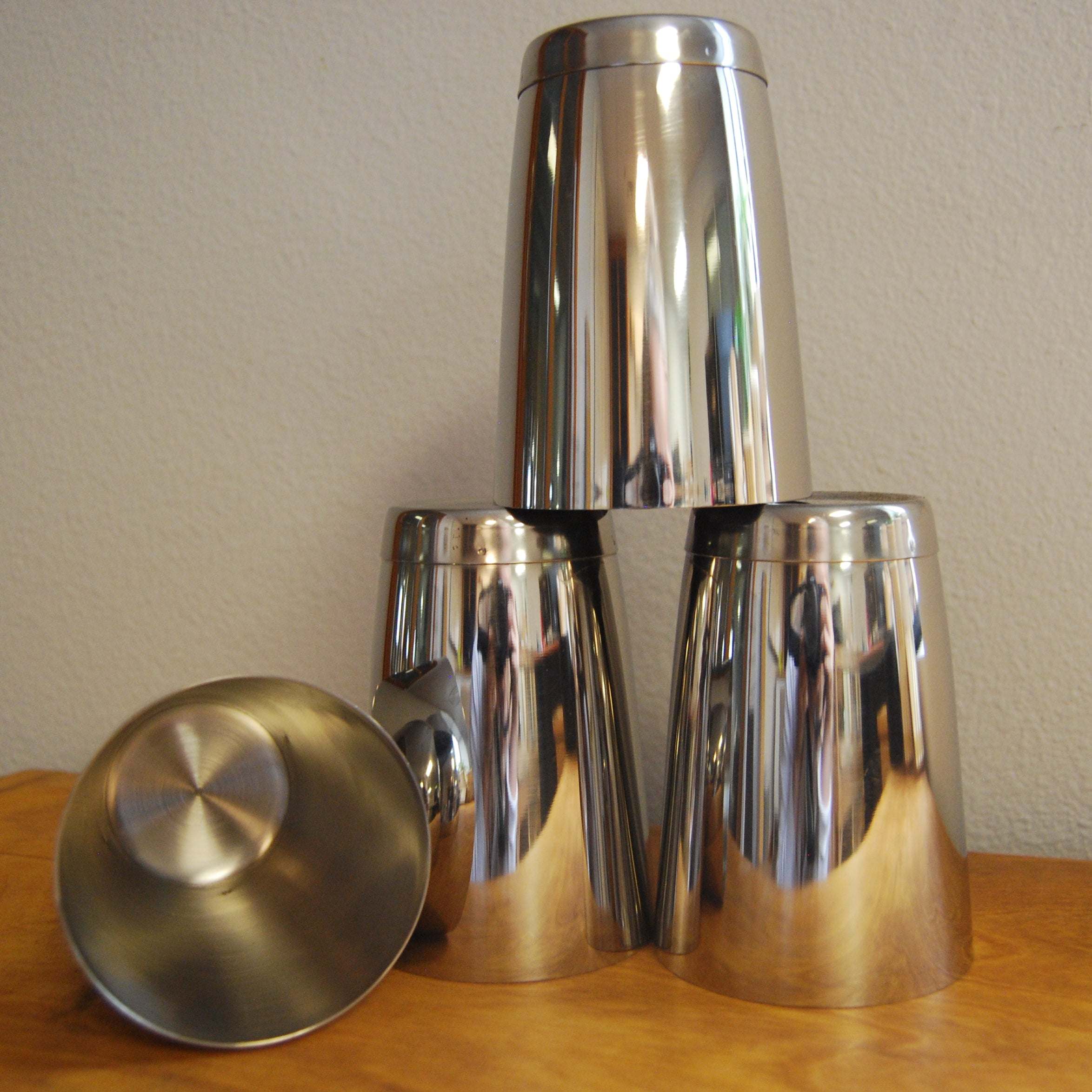 Stack of four shiny, tapered stainless steel cups arranged on a wooden surface.
