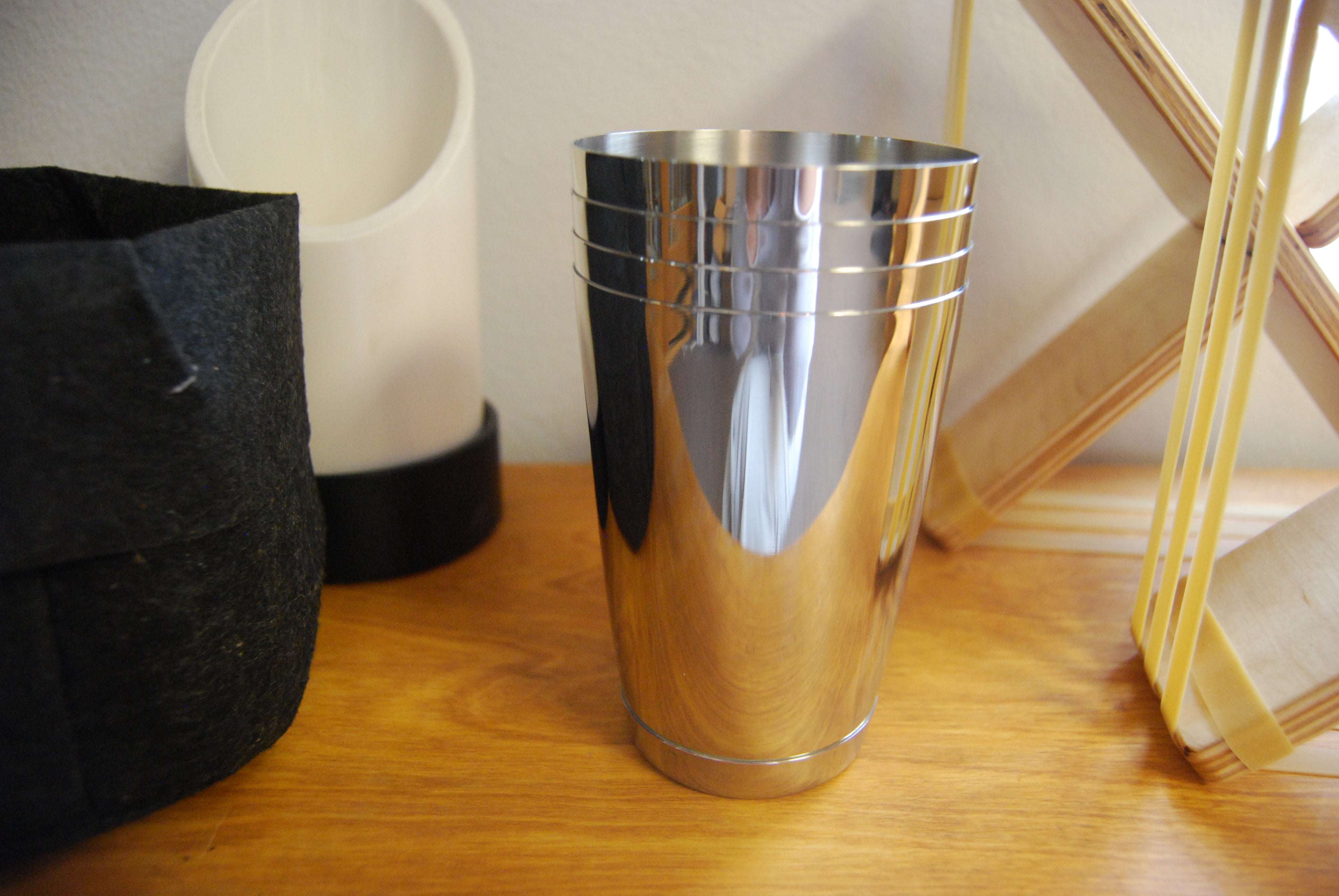 Stack of three shiny, polished stainless steel cups with horizontal ribbed detailing on a wooden surface.