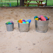 Children using metal pails for outdoor learning activities with soil and rocks