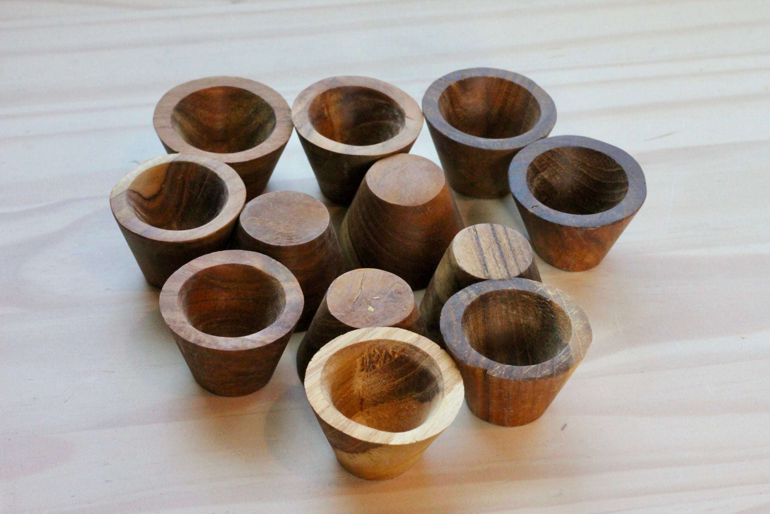 Set of small, natural wooden bowls with a tapered design arranged on a light wooden surface.