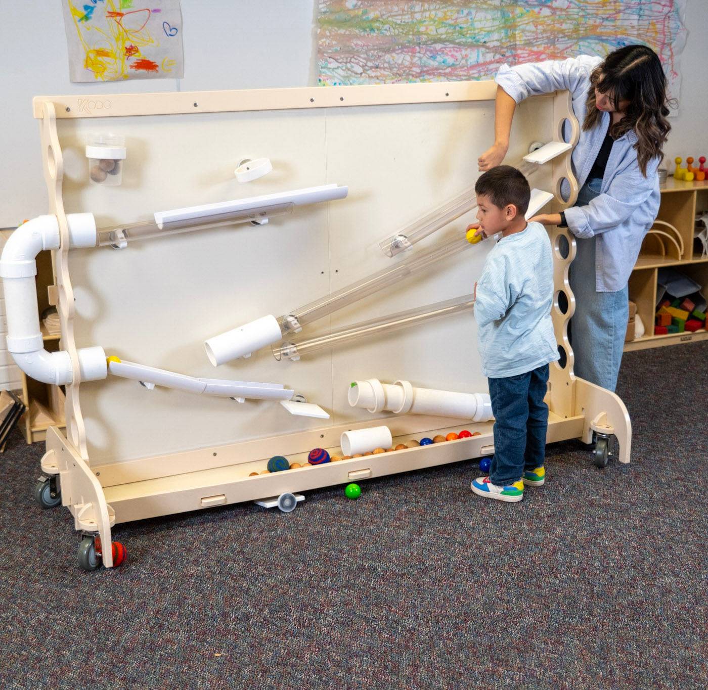 Teacher and child playing with a mobile Baltic birch STEM magnet wall featuring magnetic ramps and tubes.