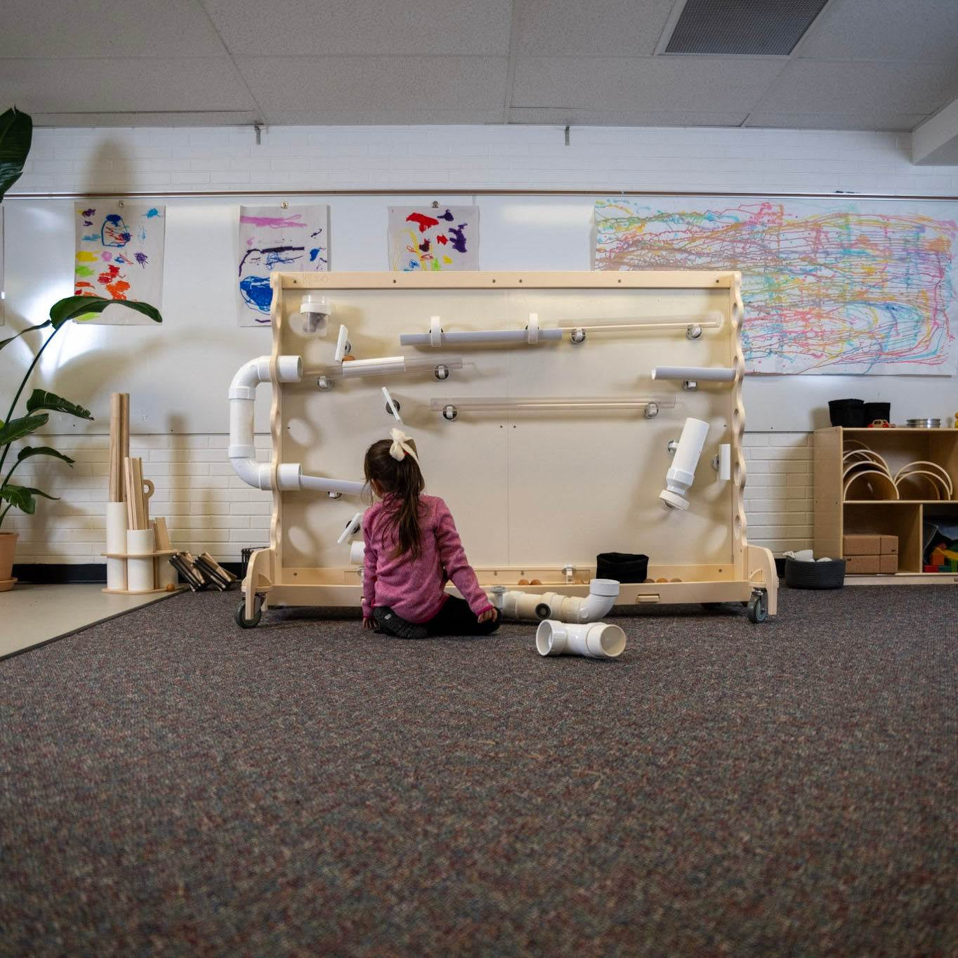 Child playing with a portable Baltic Birch STEM magnet wall featuring magnetic pipes and ramps on a rolling stand.