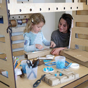 Child and teacher using a light wood Mobile Maker Station with storage bins, tools, and a large tabletop for STEM projects.