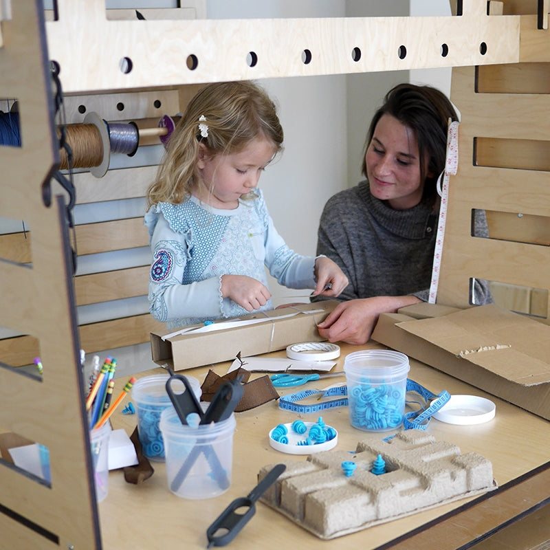 Child and teacher using a light wood Mobile Maker Station with storage bins, tools, and a large tabletop for STEM projects.