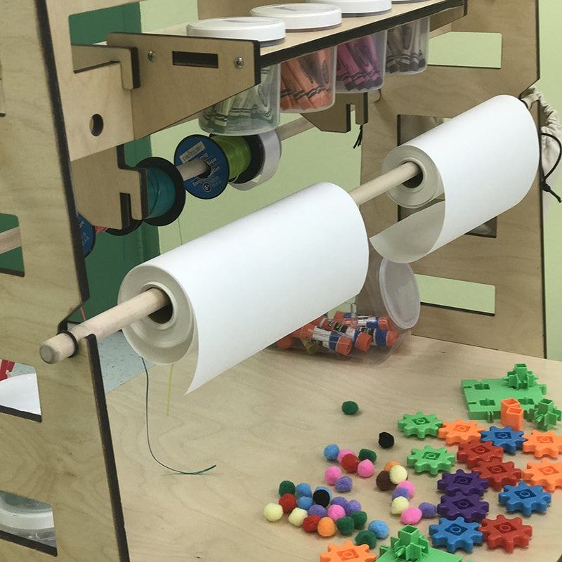 Mobile maker station with plywood frame, paper roll dispensers, storage bins, and colorful STEM building gears.