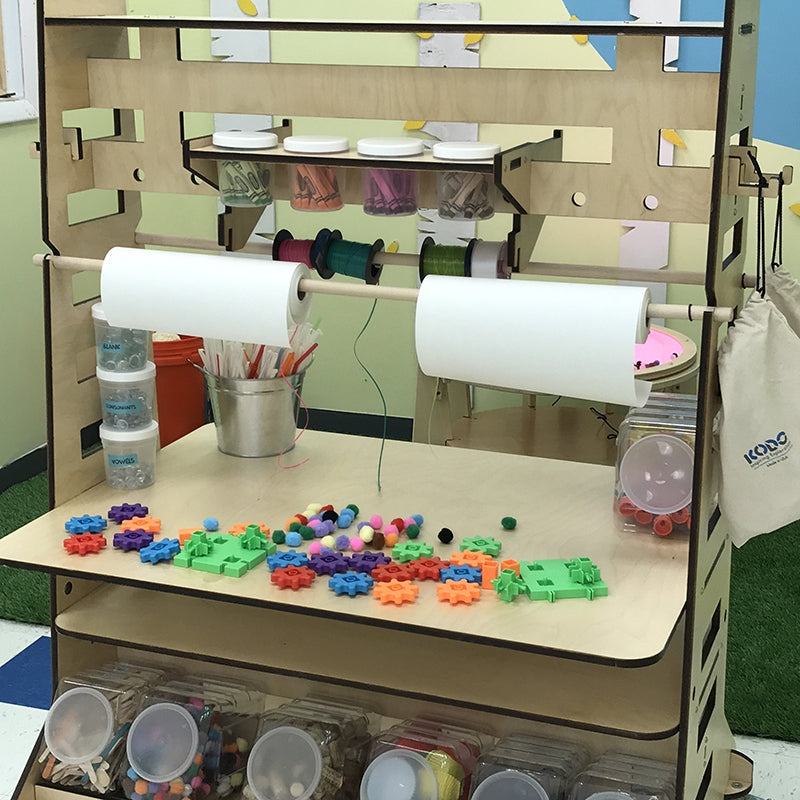 Mobile wooden maker station with tabletop, paper rolls, storage bins, and colorful STEM building parts for classrooms.