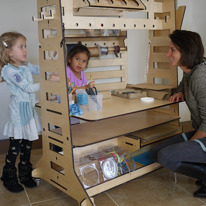 Mobile maker station cart made of light wood with storage shelves and a workspace, used by children and an adult.