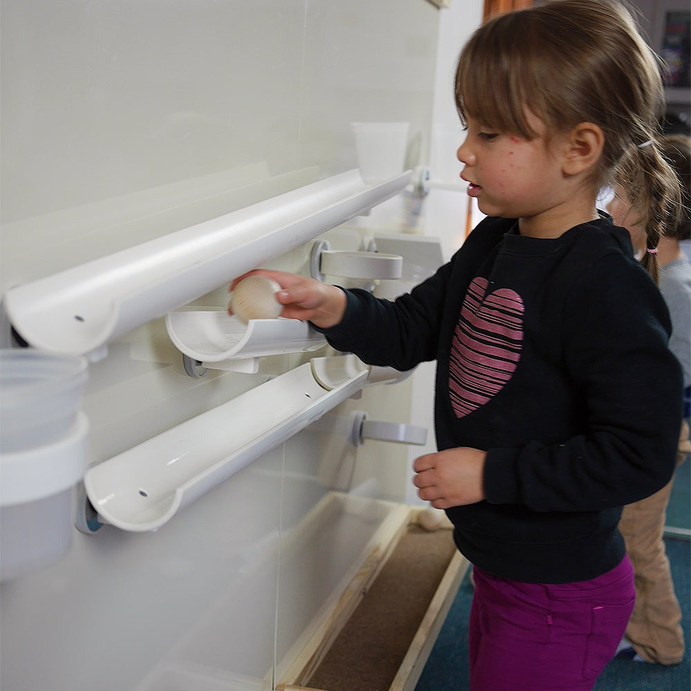 Child placing a ball on white magnetic ramps attached to a vertical wall for physics experiments.