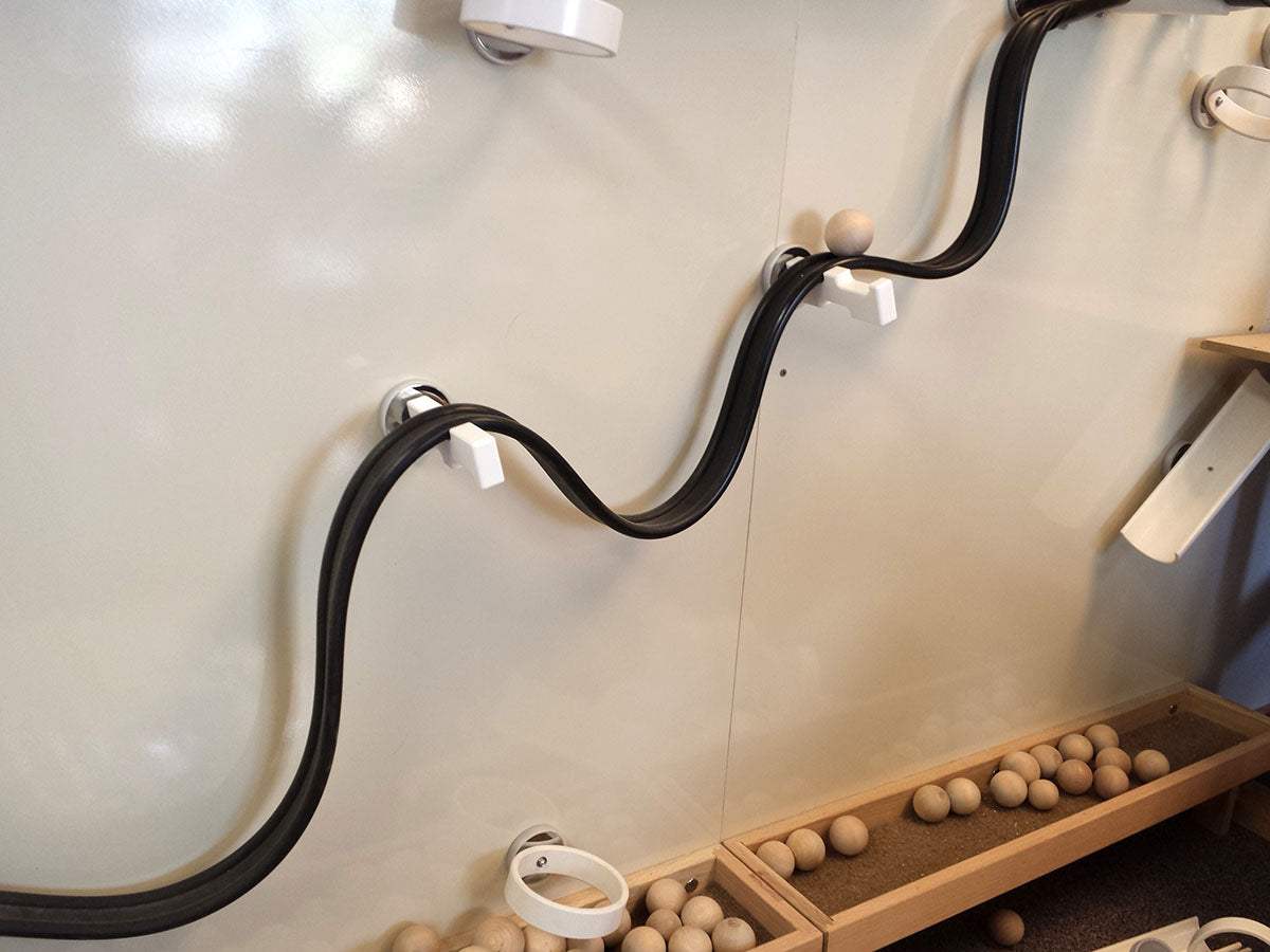 Black magnetic track mounted on a white wall with wooden balls for physics experiments.
