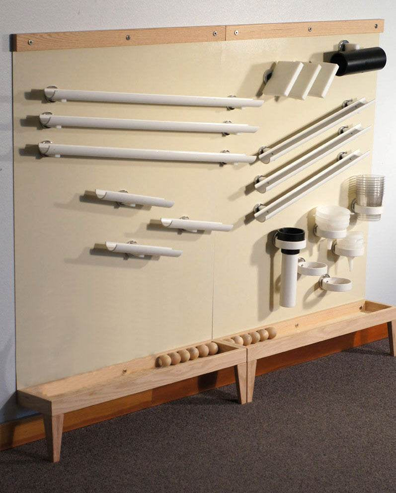 Beige vertical magnetic wall with wooden trim, featuring various white plastic ramps, tubes, and cups for physics experiments.