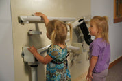 Children playing with white magnetic ramps and tracks on a beige vertical museum wall.