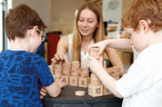 Children and teacher playing with a wooden number stacker set featuring numerals and dot arrays on beech wood blocks.