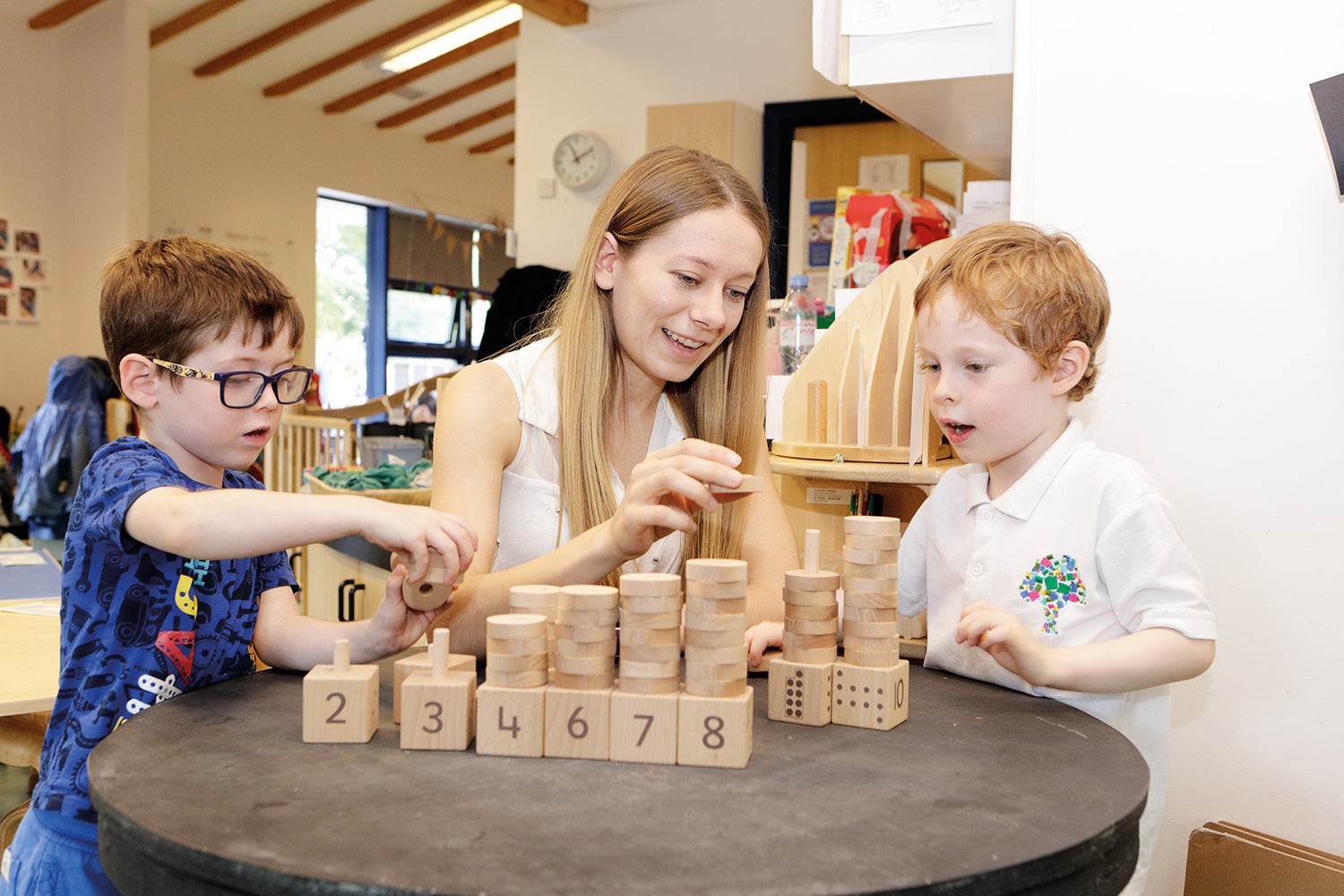 Teacher and children playing with a wooden Natural Number Stacker set featuring numbered blocks and stacking discs.