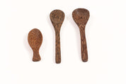 Three handcrafted spoons made from dark, textured coconut shell with unique wood grain patterns on a white background.