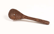 Small brown spoon made from natural coconut shell with a smooth, wood-grain texture and a single hole in the bowl.