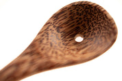 Close-up of a sustainable coconut shell spoon with a natural wood grain pattern and a small hole in the bowl.