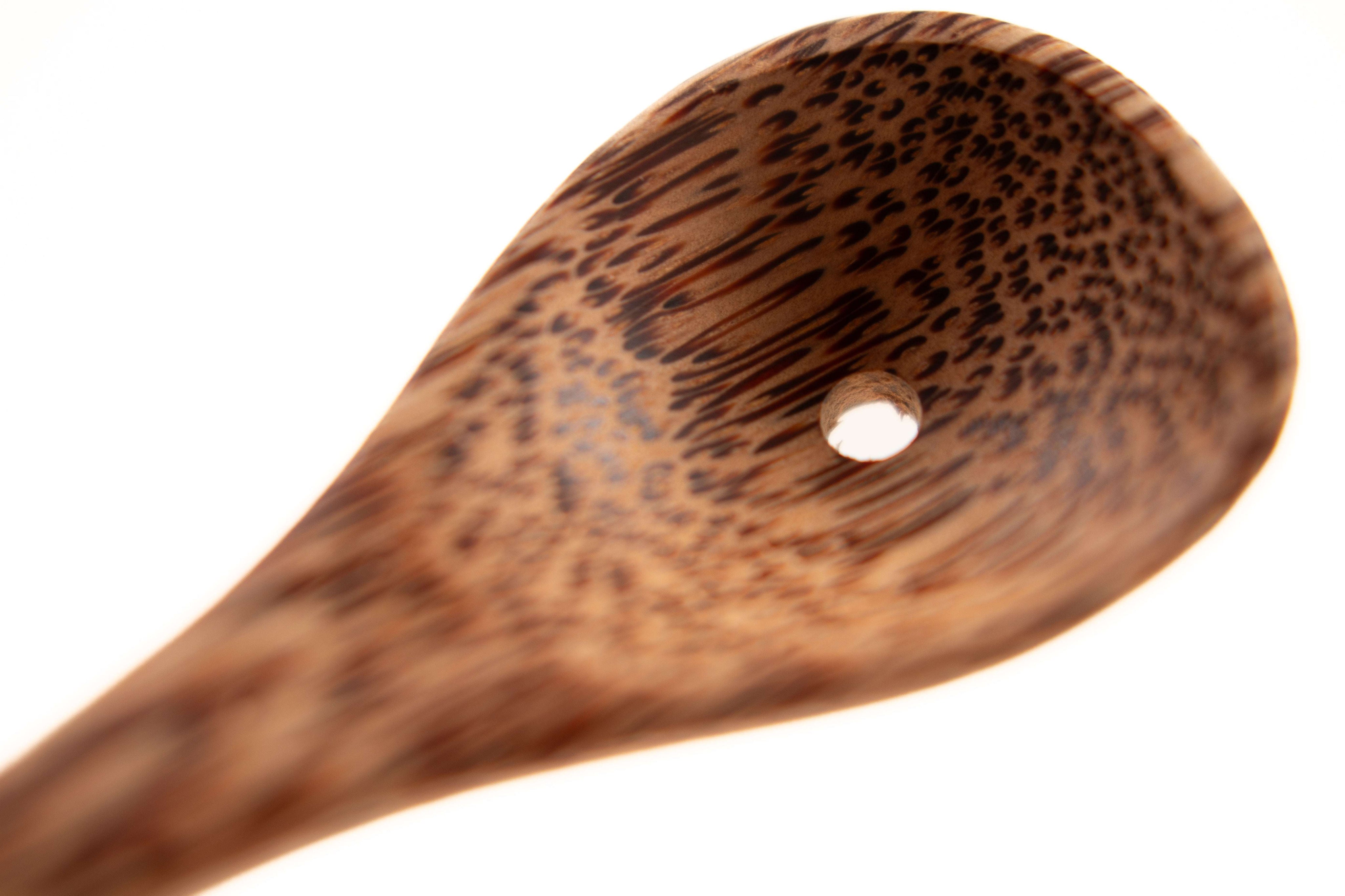 Close-up of a sustainable coconut shell spoon with a natural wood grain pattern and a small hole in the bowl.