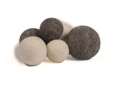A cluster of soft, round, undyed natural wool balls in varying shades of cream, grey, and charcoal on a white background.