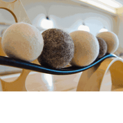 Set of soft, undyed natural wool balls in shades of cream and brown resting on a curved wooden educational ramp.