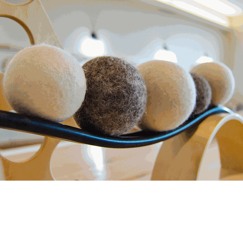 Set of soft, undyed natural wool balls in shades of cream and brown resting on a curved wooden educational ramp.