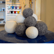 Stack of soft, round, natural wool balls in contrasting grey and cream colors on a blue surface.