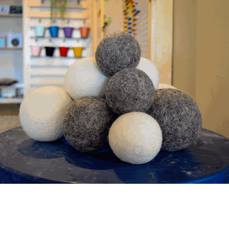 Stack of soft, round, natural wool balls in contrasting grey and cream colors on a blue surface.