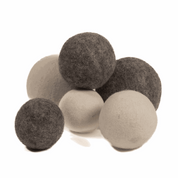 A cluster of soft, round, undyed natural wool balls in varying shades of light cream and dark charcoal grey.