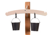 Outdoor balance scale with a beige metal arm mounted on a wooden post, featuring two hanging galvanized steel pails.