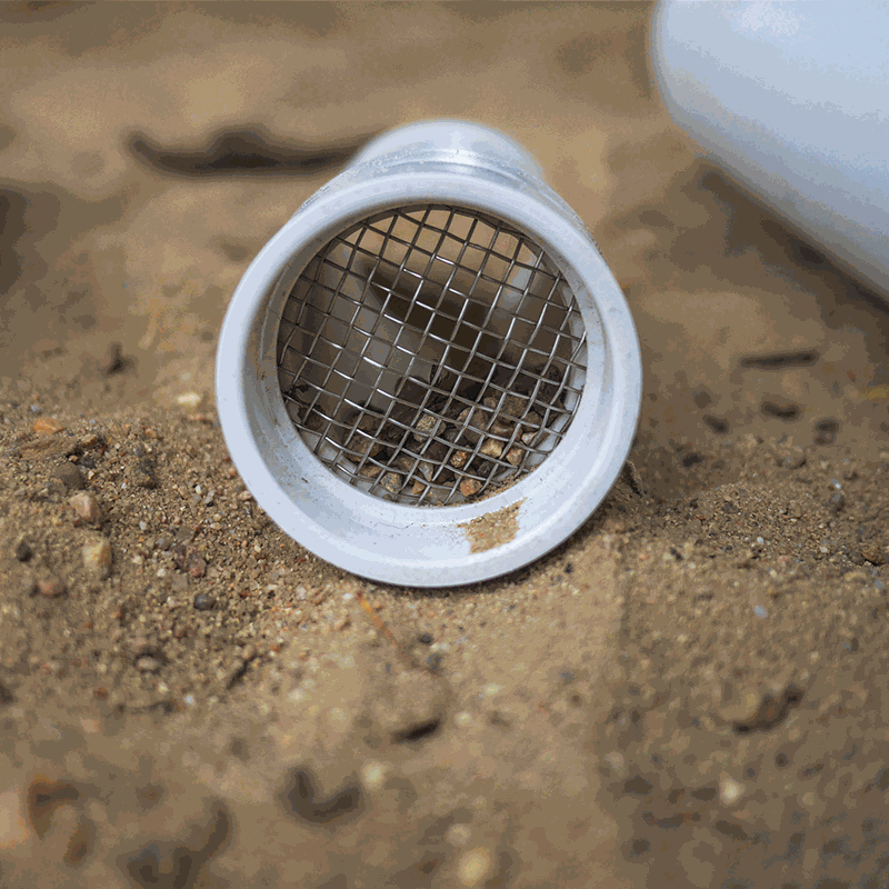 White plastic outdoor sifter scoop with a metal mesh screen resting on sandy ground.