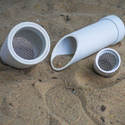 Three white plastic outdoor sifter scoops of varying sizes with metal mesh screens resting in sand.