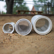 Three white cylindrical outdoor sifter scoops with metal mesh screens resting in a sandbox.