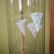 White paper cone cups with decorative green marker designs floating inside a clear vertical wind tunnel.
