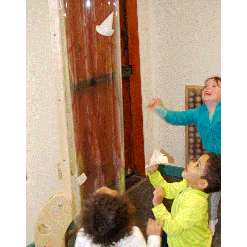 Children watching a white paper cone cup float inside a vertical clear plastic wind tunnel tube.