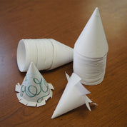 Stacks of white paper cone cups on a wooden table, including two decorated with cut flaps and marker designs.